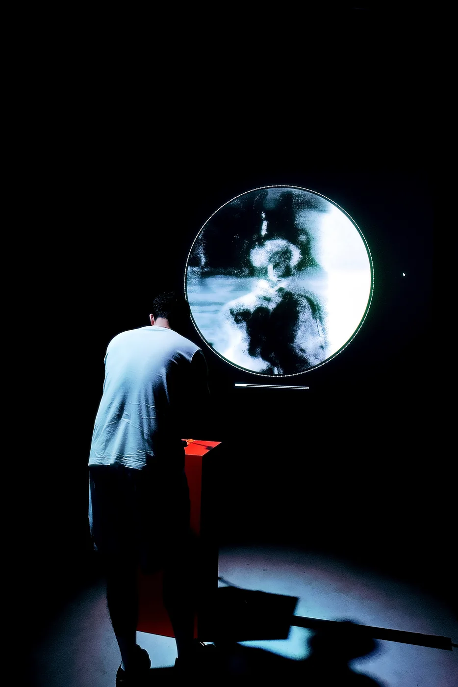 A visitor stands at the red podium facing the circular memory projection
